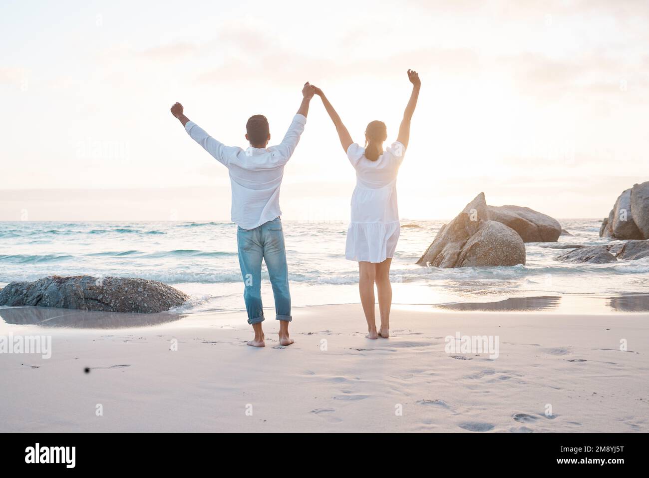 Ein Gefühl der Zugehörigkeit ist eine wunderbare Sache. Ein junges Paar stand mit erhobenen Händen am Strand. Stockfoto