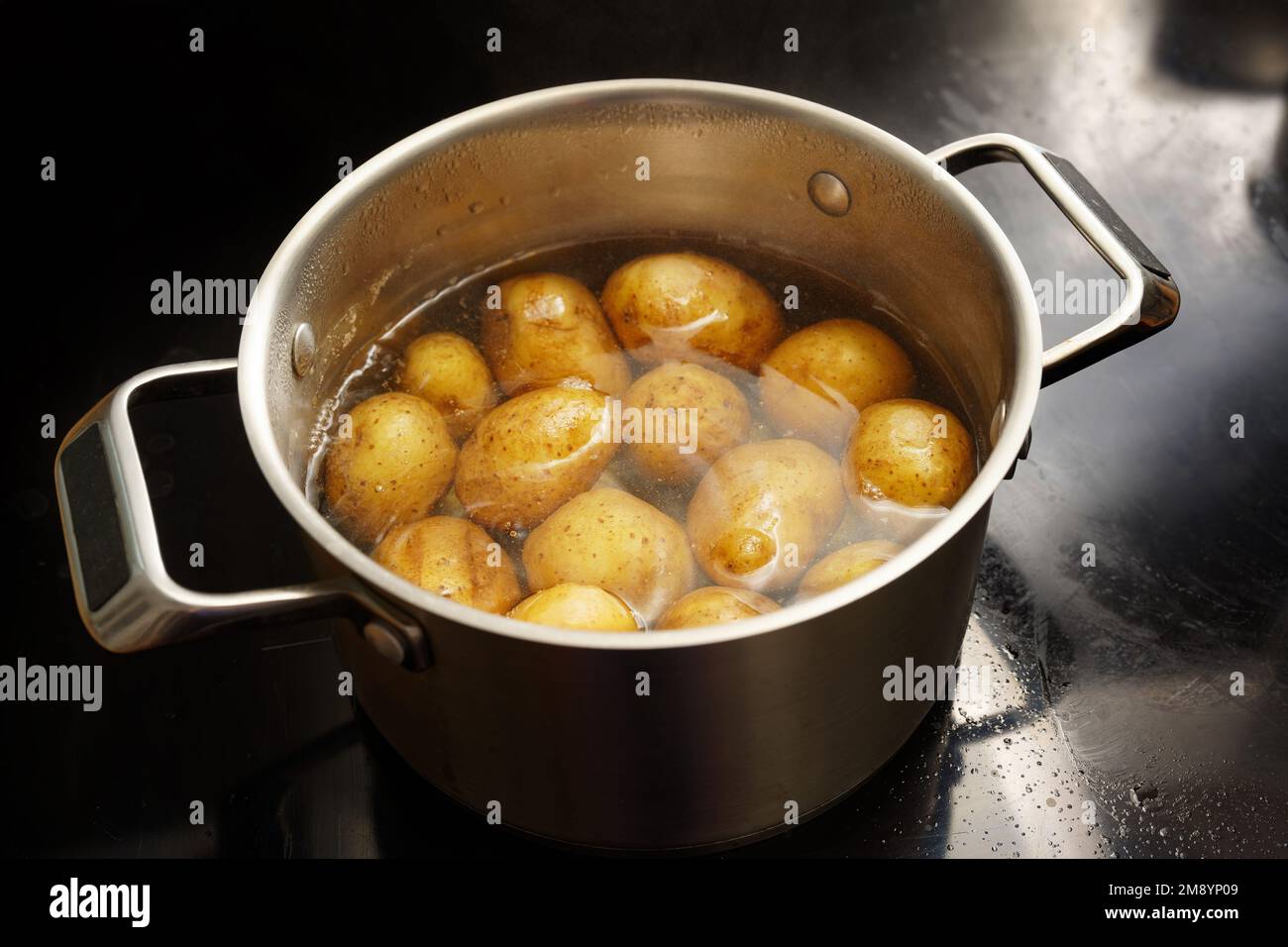 Kartoffeln mit Schale in einem Edelstahltopf mit kochendem Wasser auf dem Herd, gesundes Kochkonzept, Kopierraum, ausgewählter Fokus, geringe Falltiefe Stockfoto