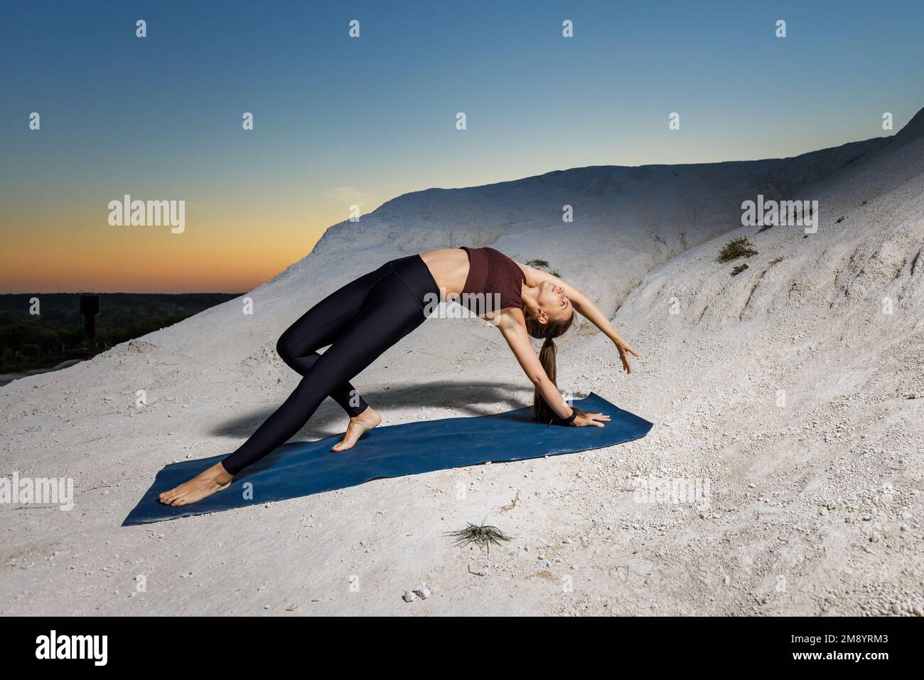 Junge schlanke Frau, die Joga macht und bei Sonnenuntergang draußen auf der Matte posiert Stockfoto