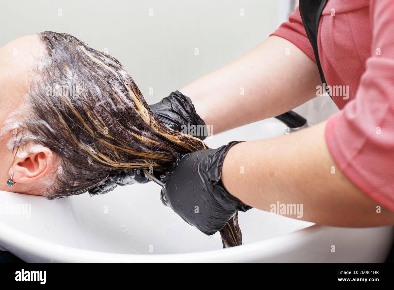 Der Friseur in schwarzen Handschuhen wäscht die Haare der braunen Frau im Schönheitssalon Stockfoto