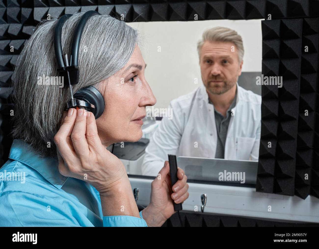 Hörtest. Patientin mit audiologischen Kopfhörern drückt auf Tastendruck während der audiometrischen Prüfung in einer schalldichten Audiologiekabine Stockfoto