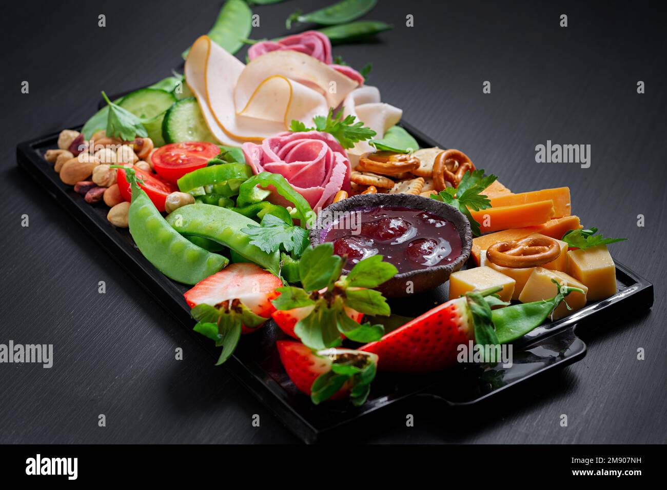 Vorspeisenplatte kaltgeschnittener Schinken, Salami, Cracker, Erdbeeren, Gemüse und Käseplatte an Bord vor dunklem Hintergrund. Vorspeisentisch mit Stockfoto