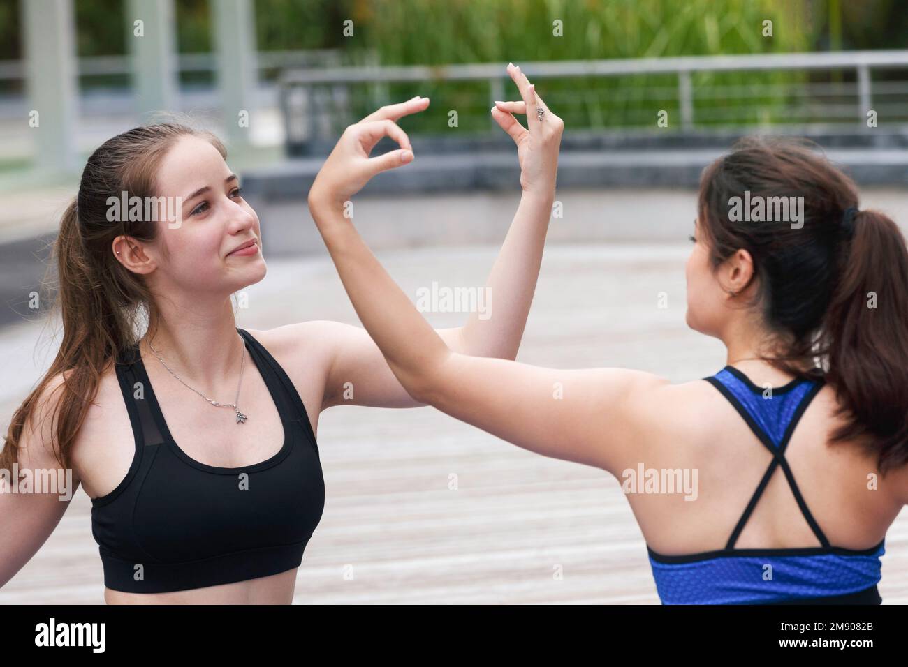 Zwei fröhlich lächelnde, wunderschöne weibliche Teenager-Freunde üben am Wochenende Yoga-Übungen im Stadtpark im Freien. Gesunder Bewegungssport und Lifest Stockfoto