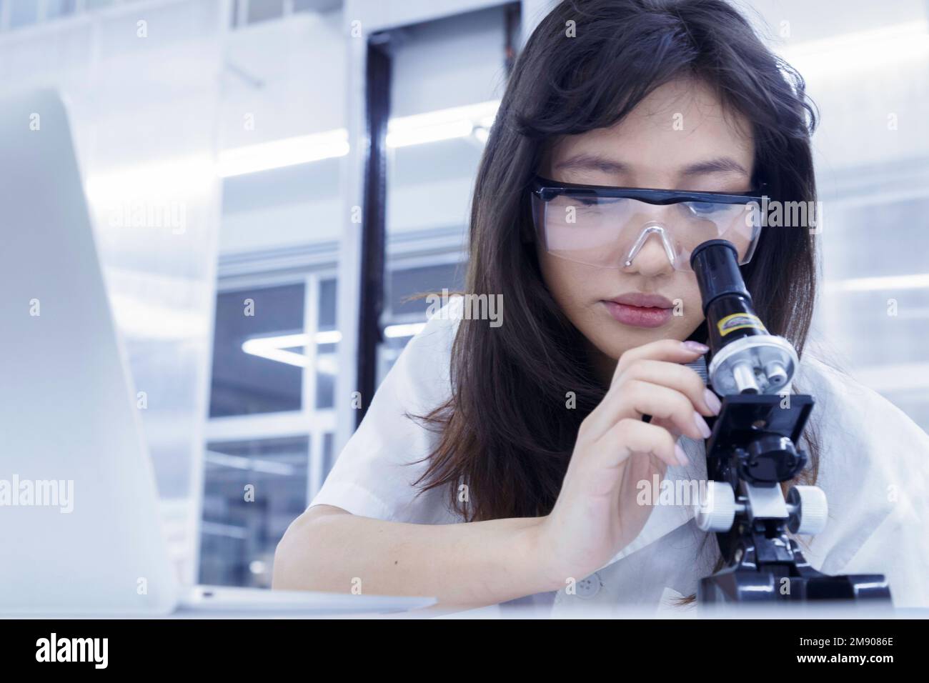 Arztstudentin untersucht und analysiert Virusprobe auf dem Mikroskop. Junger Biotechnologie-Spezialist im Labor. Medizinisch-wissenschaftlicher Laborateur Stockfoto