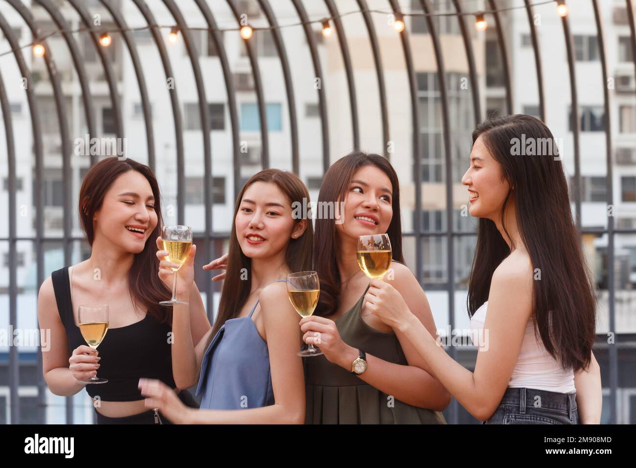 Glückliche asiatische Teenager jubeln und stoßen mit weißem Sektglas an, um auf der Dinnerparty im Sommer zu feiern. Feier, Beziehung Stockfoto