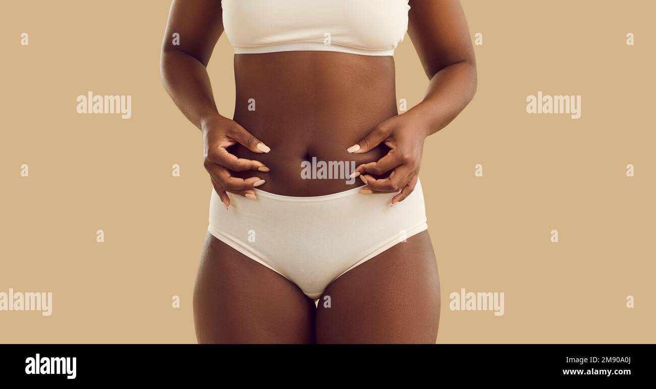 Eine schwarze Frau mit Körperfett kneift sich den Bauch, isoliert auf beigefarbenem Hintergrund Stockfoto
