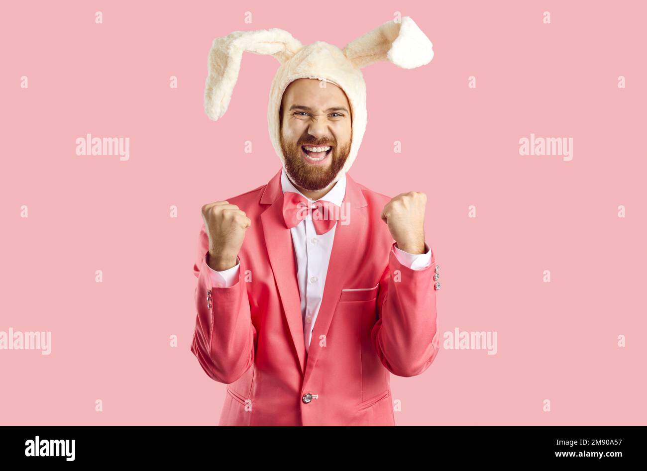 Positiv aufgeregter Mann mit Hut und Kaninchenohren freut sich über sein Glück, isoliert auf pinkfarbenem Hintergrund. Stockfoto