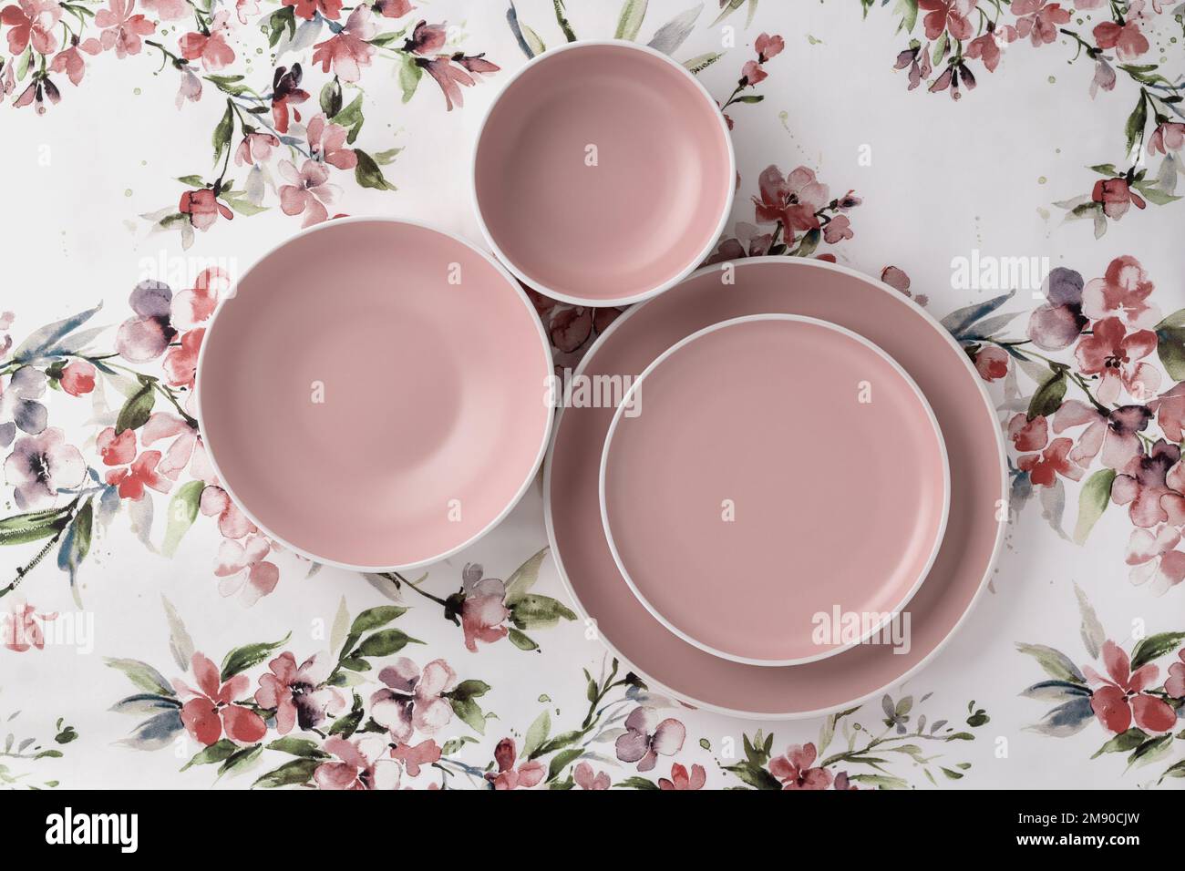 Leere saubere Teller auf einer weißen Tischdecke mit Blumenmuster, Blick von der Tischplatte. Flach liegend, minimalistisches Design. Rosafarbenes Keramikgeschirr. Trendiges Geschirr Stockfoto
