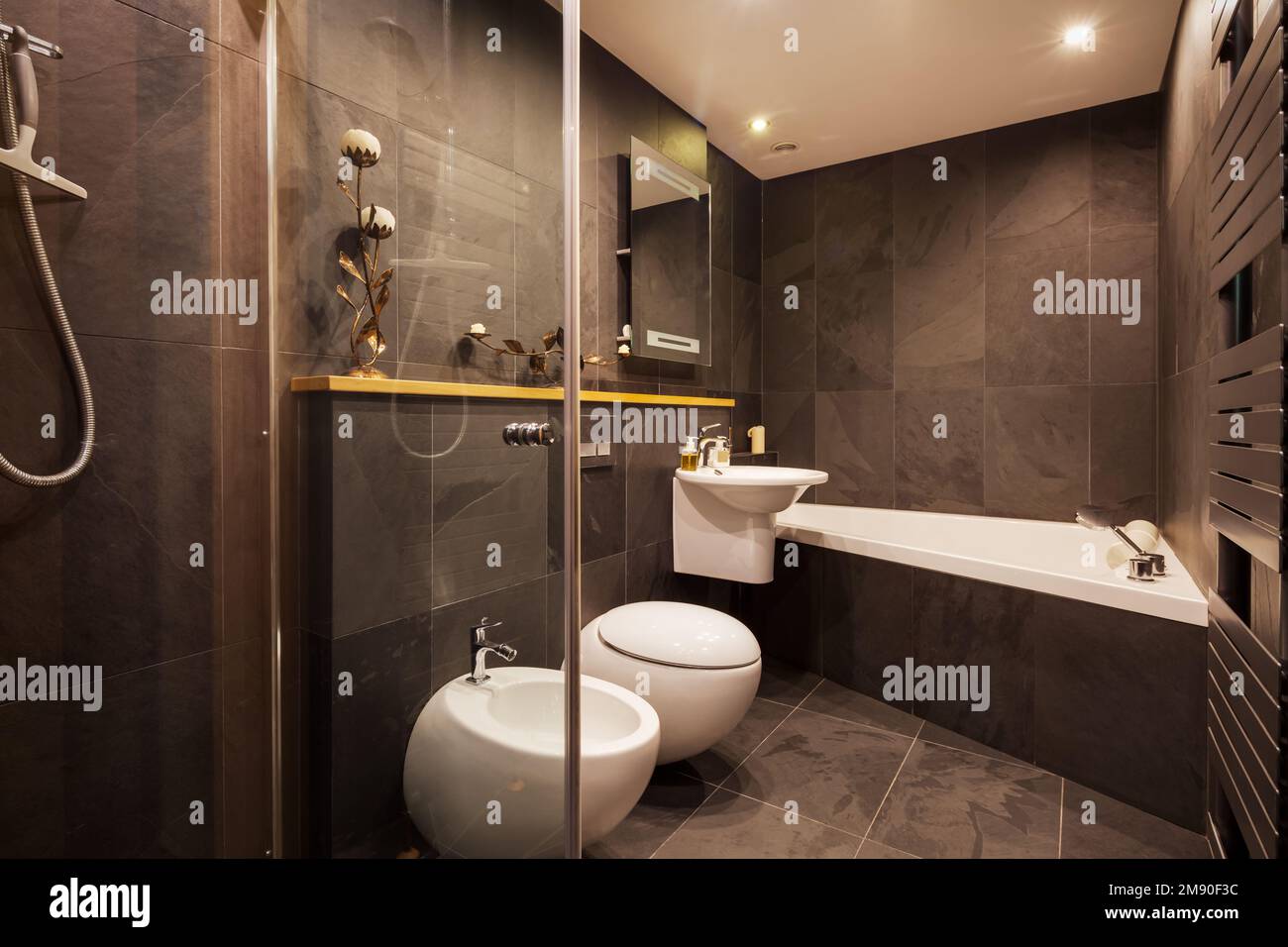 Modernes gefliestes Badezimmer mit dunklen gefliesten Wänden, beheiztem Handtuchhalter und modernen Armaturen Stockfoto
