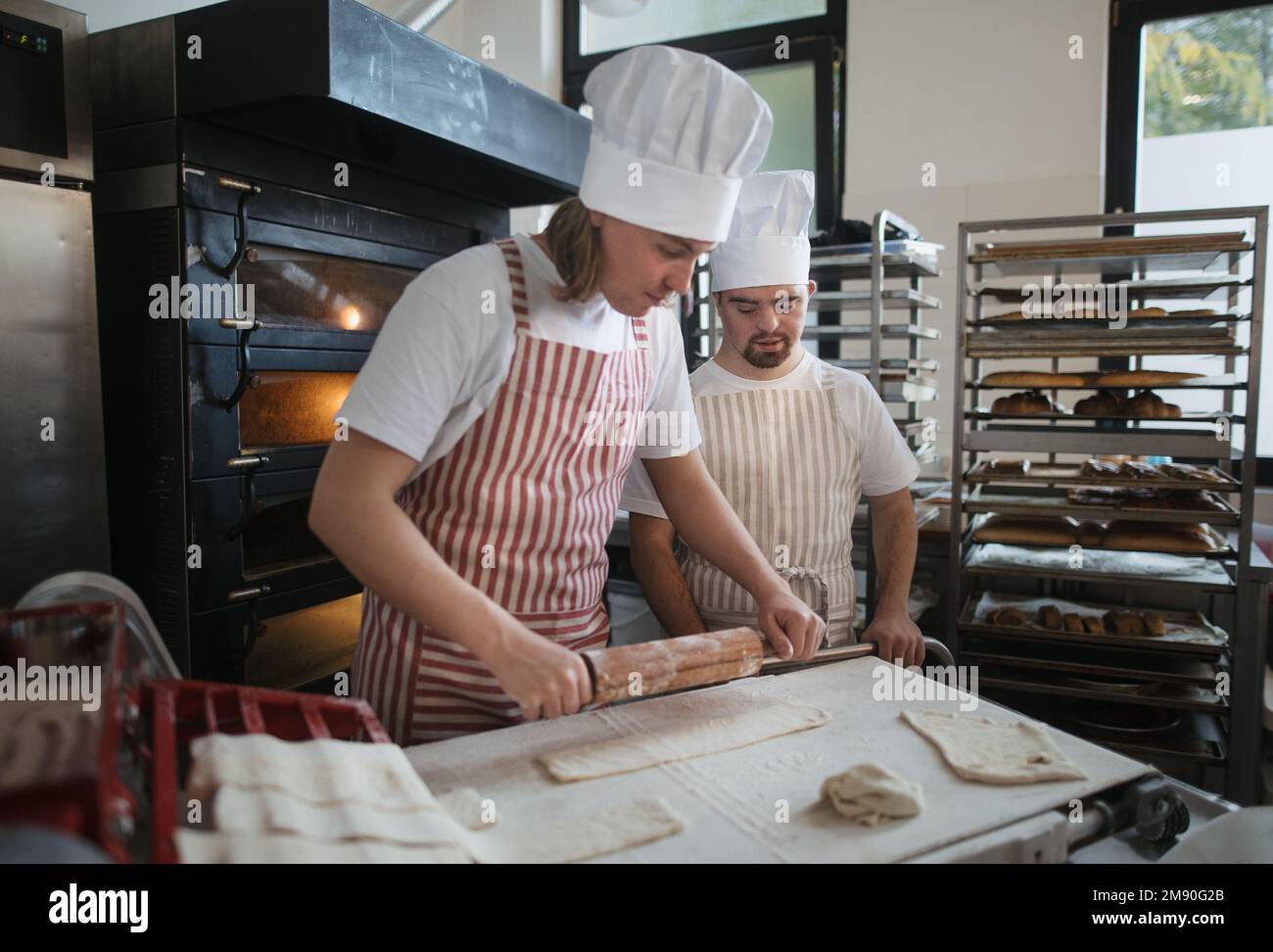 Ein Mann mit daunensyndrom, der mit seinem Kollegen Brot in der Bäckerei vorbereitete. Konzept der Integration von Menschen mit Behinderungen in die Gesellschaft. Stockfoto