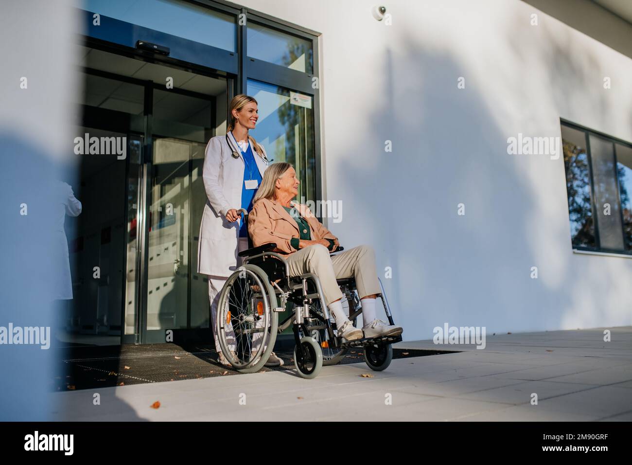 Junge Ärztin, die sich um ältere Frauen im Rollstuhl kümmert. Stockfoto