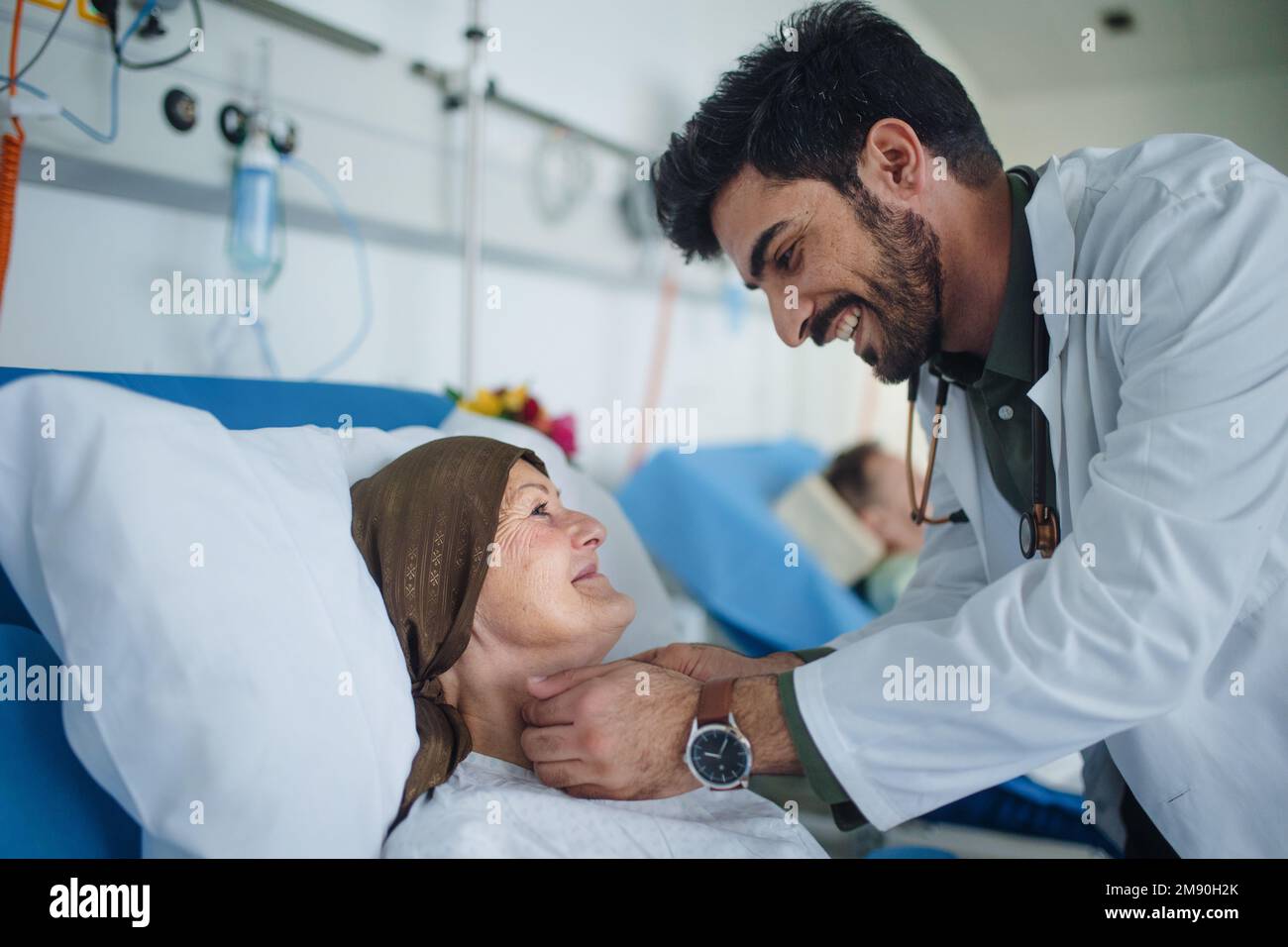 Junger Arzt aus dem Nahen Osten, der während der Untersuchung von Patienten im Krankenzimmer lächelt. Stockfoto