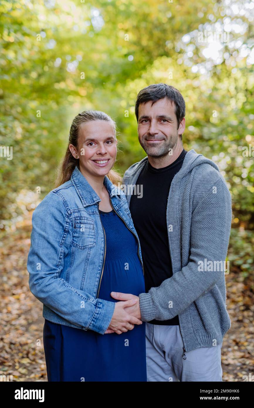 Porträt einer glücklichen schwangeren Frau und ihres Mannes, die im Wald stehen. Stockfoto