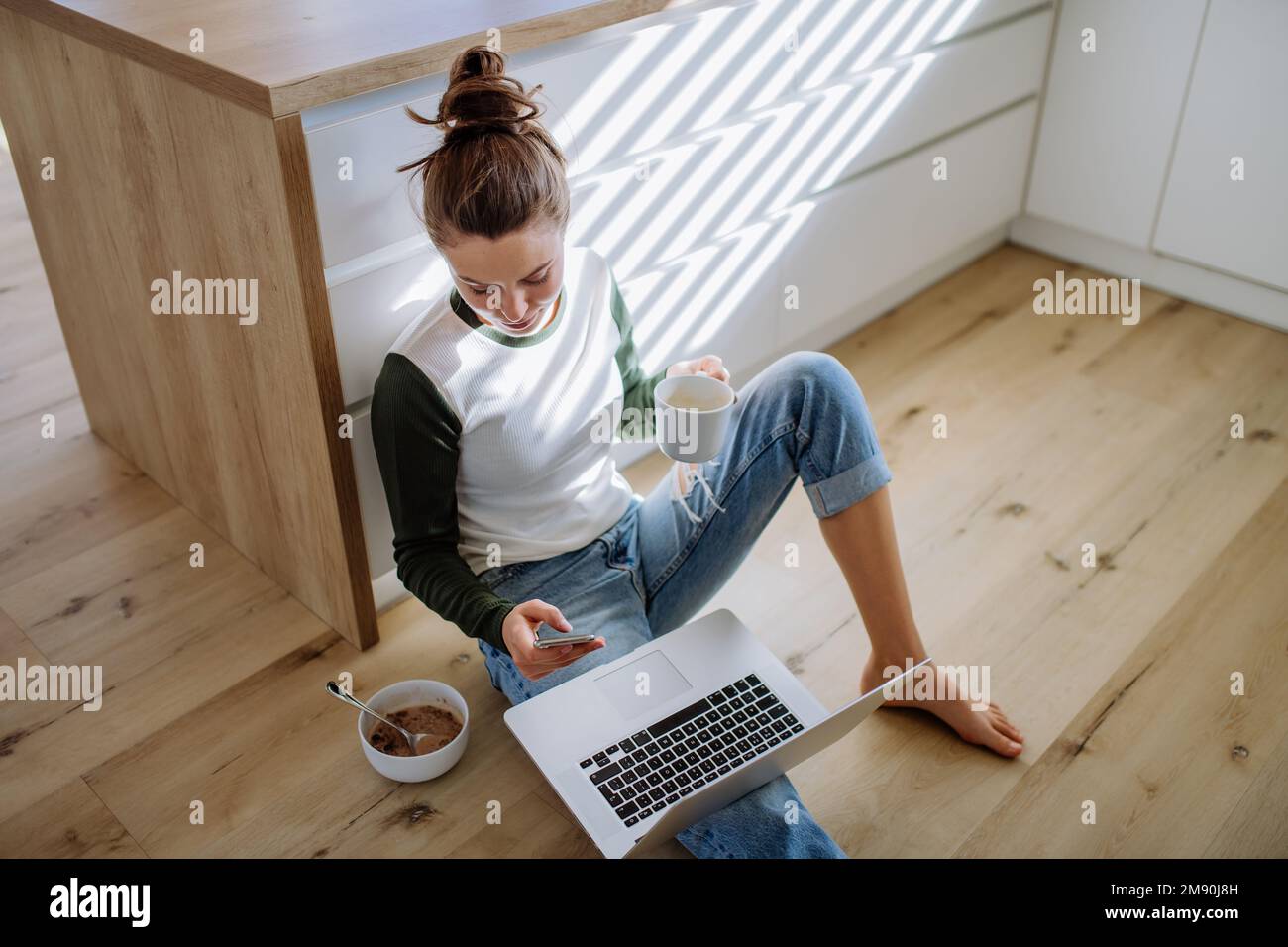 Junge Frau, die mit einem Laptop und einer Tasse Kaffee in der Küche sitzt. Stockfoto