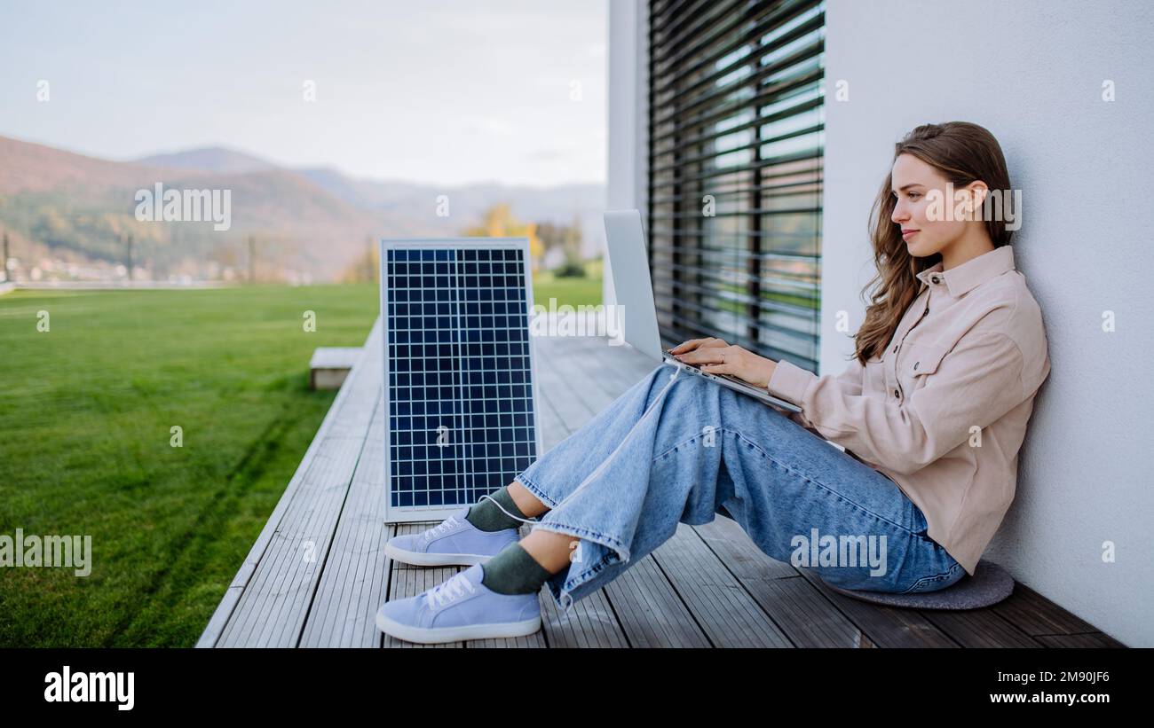 Junge Frau sitzt auf der Terrasse und lädt Tablet durch Solarpanel. Stockfoto