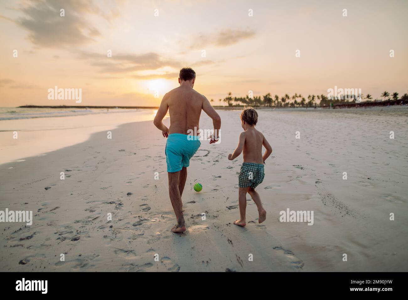 Rückansicht eines Vaters mit seinem Sohn, der am Strand Fußball spielt. Stockfoto