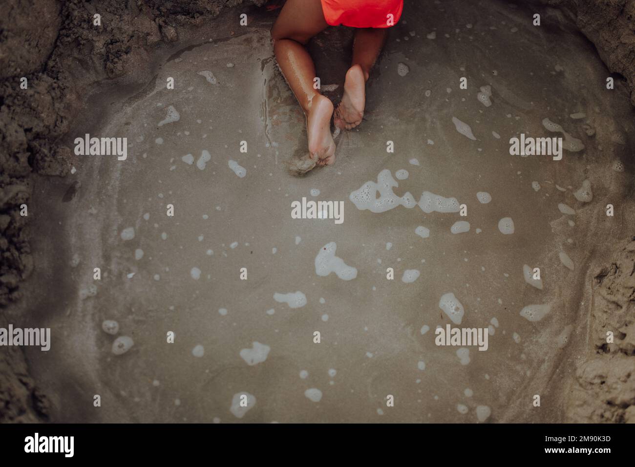 Blick von oben auf ein kleines Mädchen, das am Strand spielt und ein Loch im Sand gräbt. Stockfoto