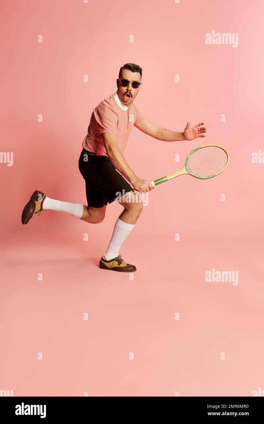 Porträts eines gutaussehenden charismatischen Mannes in stilvoller Kleidung, der mit einem Tennisschläger posiert und im pinkfarbenen Studiohintergrund spielt. Das Konzept von Mode, Sport Stockfoto