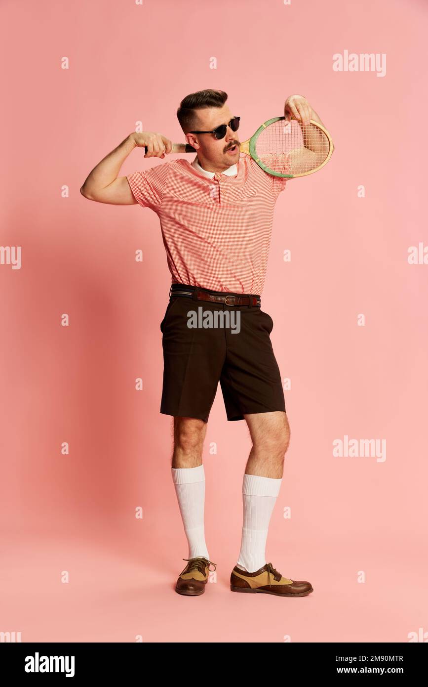 Elite-Sportverein. Porträts eines gutaussehenden charismatischen Mannes in stilvoller Kleidung mit Tennisschläger auf pinkfarbenem Studiohintergrund. Modebegriff Stockfoto
