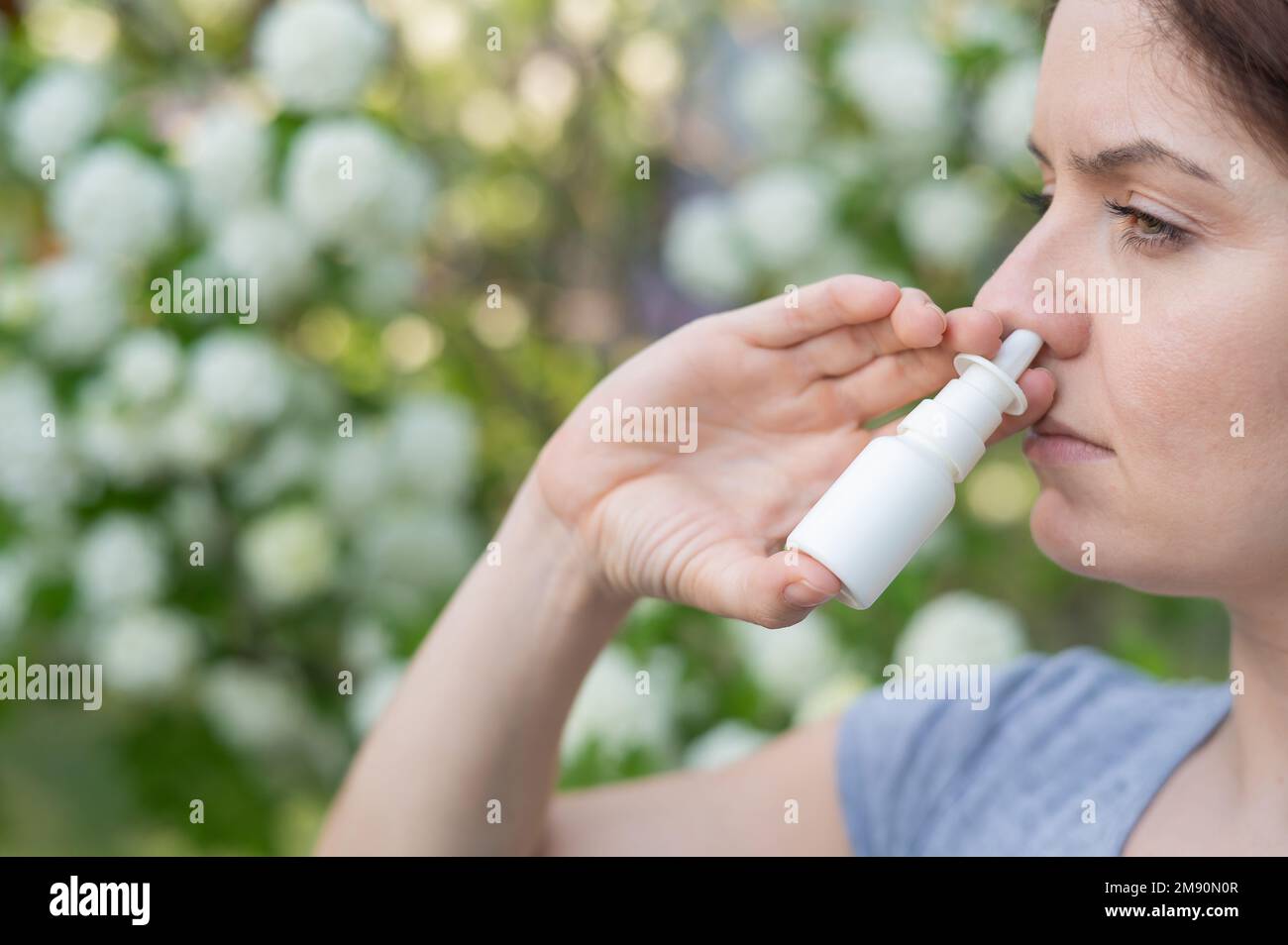 Kaukasische Frau verwendet ein Nasenspray, während sie im Park spazieren geht. Stockfoto