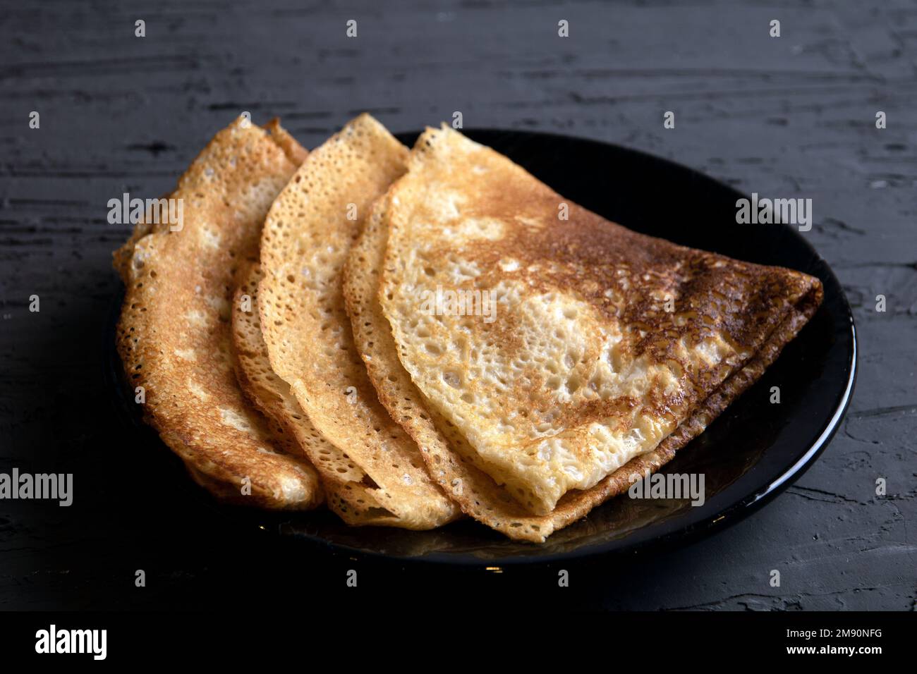 Foto von mehreren gebratenen Pfannkuchen hintereinander auf einem dunklen Teller Stockfoto