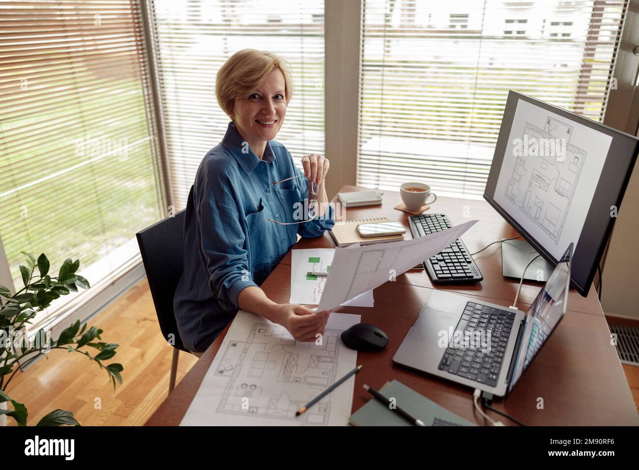 Eine lächelnde, reife Ingenieurin arbeitet vom Heimbüro aus mit einem Computer an einem Projekt Stockfoto