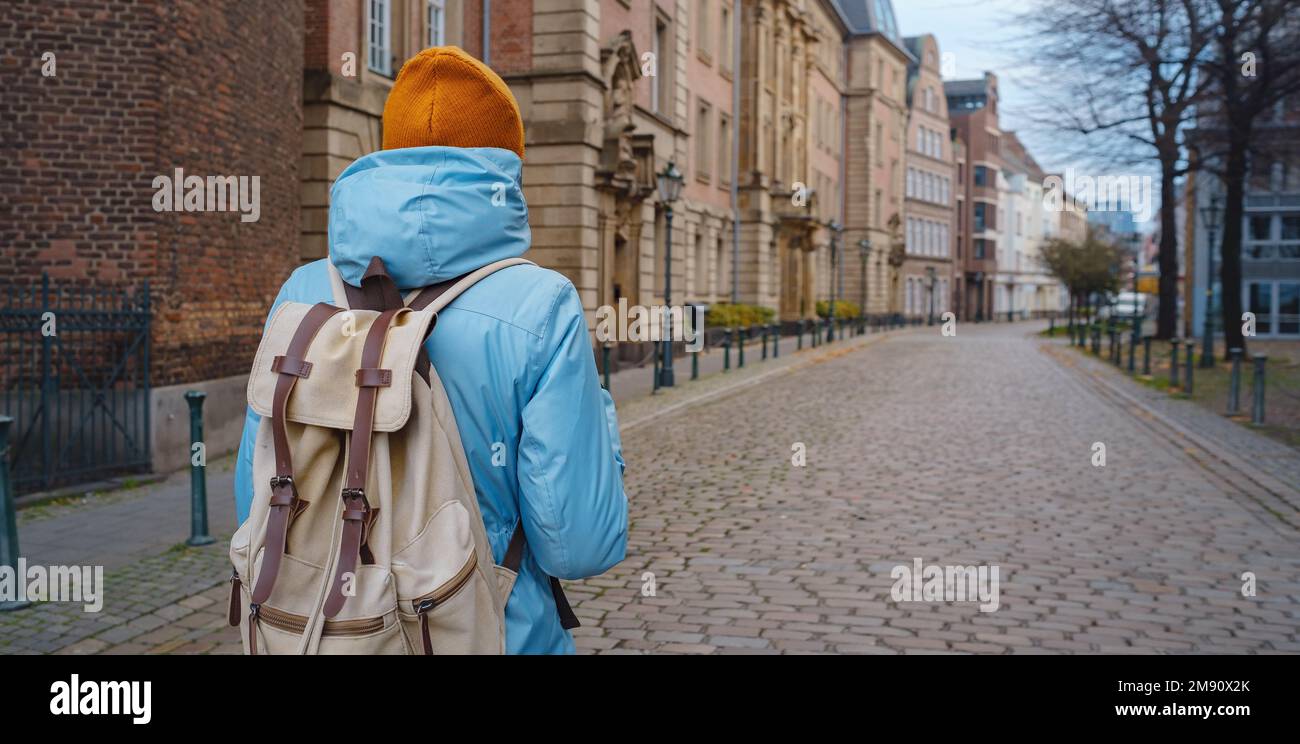 Winterreise nach Düsseldorf. Junger asiatischer Tourist in blauer Jacke und gelbem Hut (Symbol der Ukraine) spaziert durch die Sehenswürdigkeiten der Altstadt. Beliebtes Zentrum von Rheinland und Westfalen Stockfoto