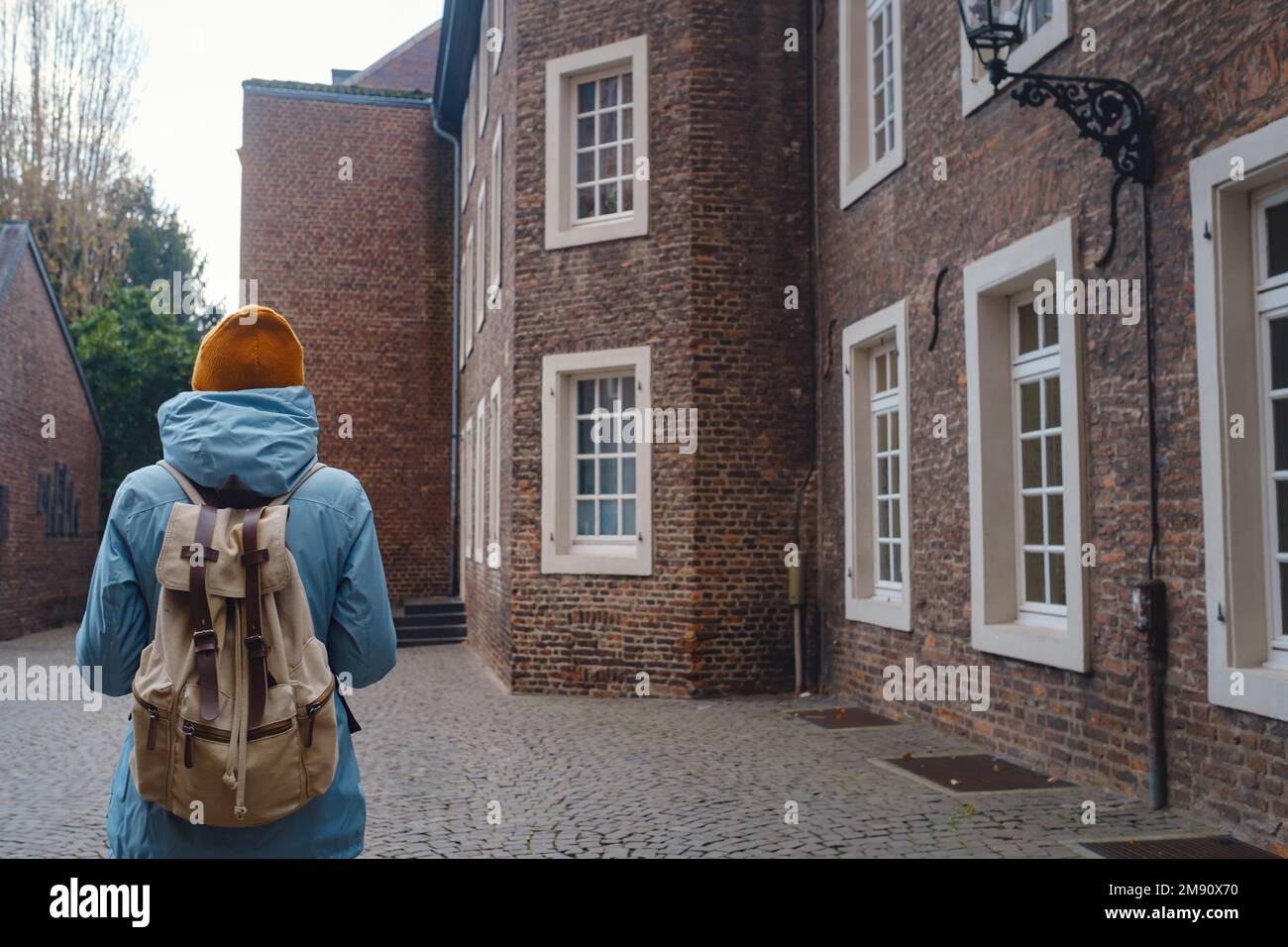 Winterreise nach Düsseldorf. Junger asiatischer Tourist in blauer Jacke und gelbem Hut (Symbol der Ukraine) spaziert durch die Sehenswürdigkeiten der Altstadt. Beliebtes Zentrum von Rheinland und Westfalen Stockfoto