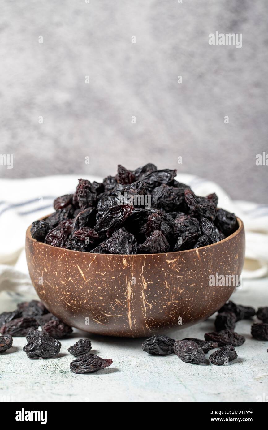 Getrocknete schwarze Trauben auf Steinhintergrund. Getrocknete Trauben in Kokosnussschale. Nusssorten. Gesunde Ernährung. Schließen Stockfoto