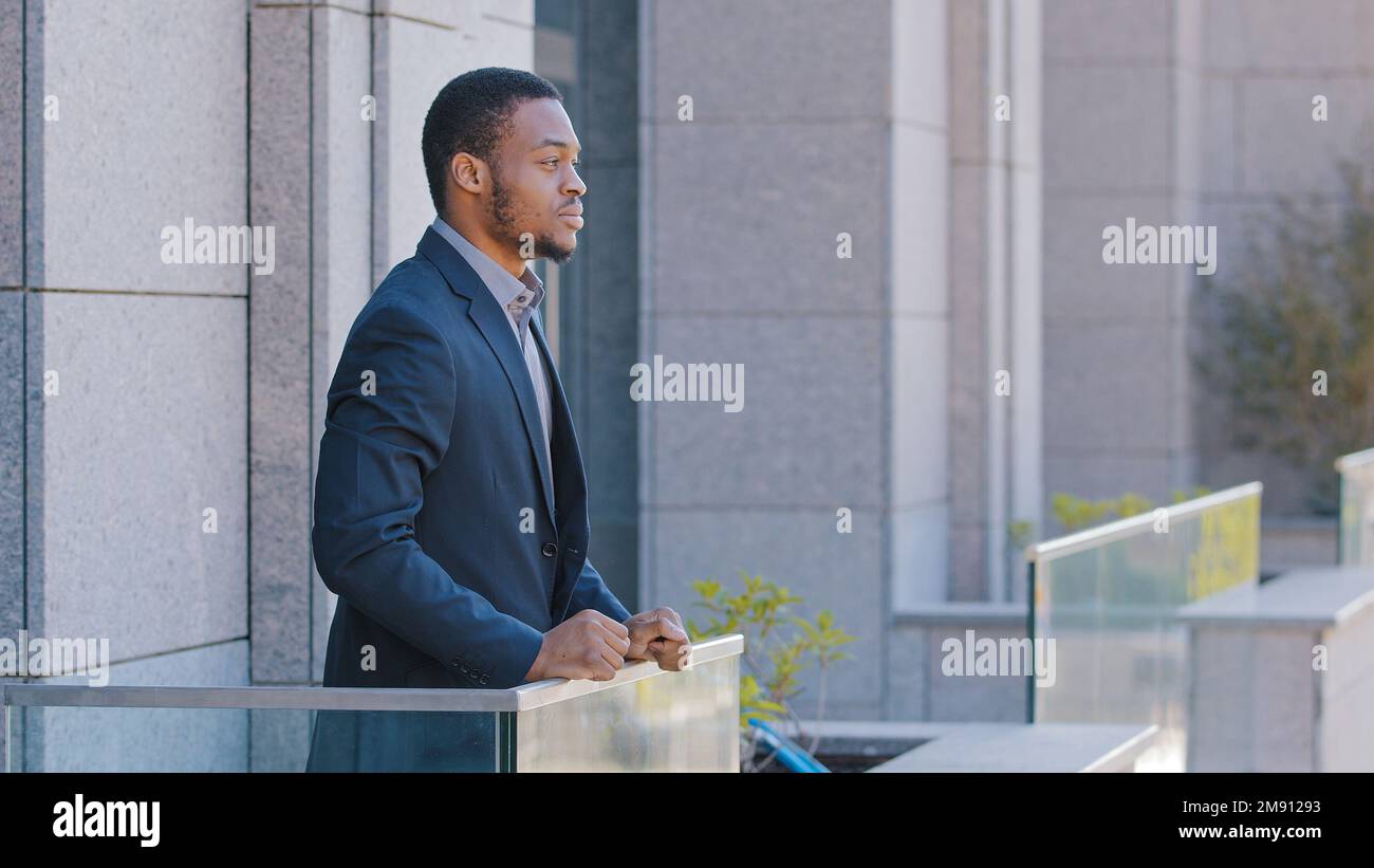 Ein afroamerikanischer Mann, der ernsthaft träumt, entspannt, aufmerksam und rücksichtsvoll, während ein Mitarbeiter im Büro auf dem Balkon steht, ethnischer Geschäftsmann, männlich Stockfoto