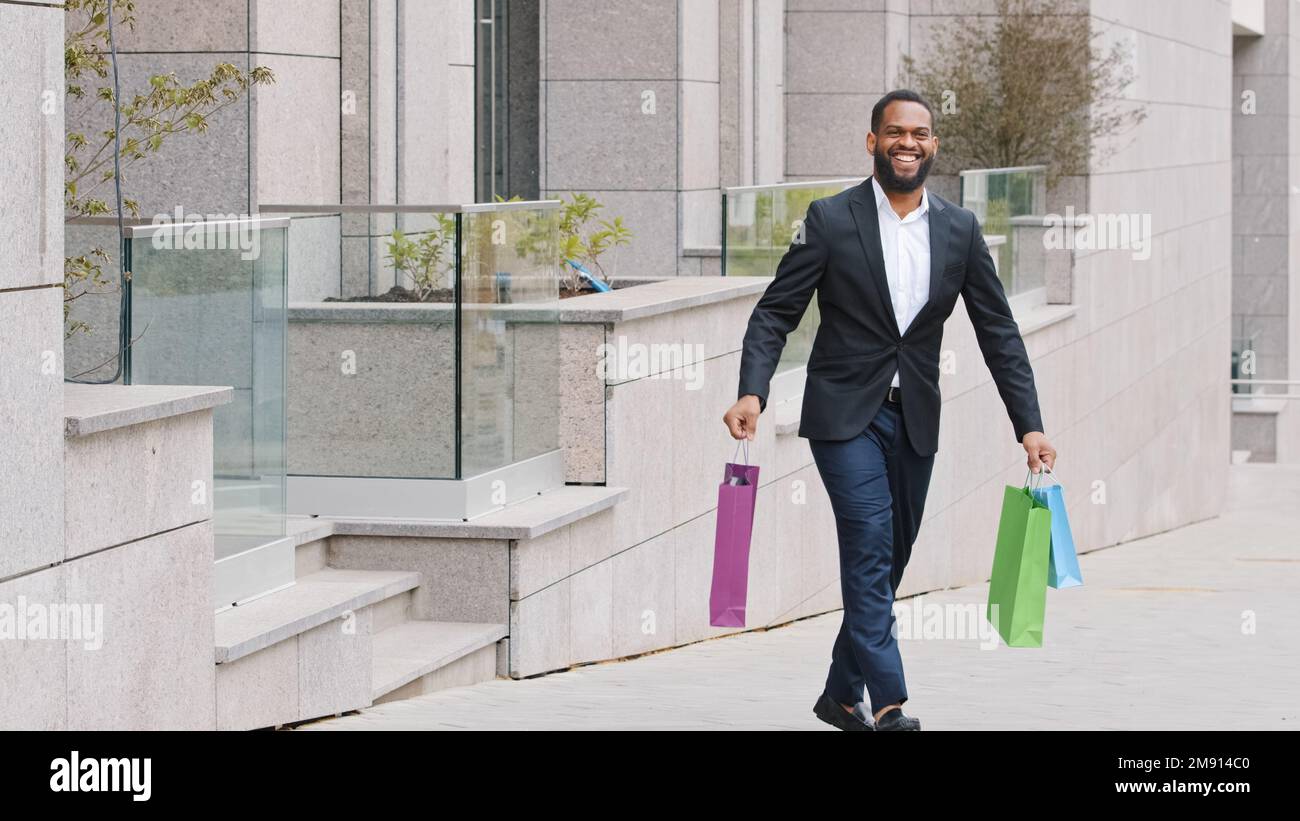Glückliche afrikanische Ethnizität ein amerikanischer Geschäftsmann mit Bart geht in der Nähe des Ladengeschäfts in der Stadt mit Einkäufen. Ein zufriedener Mann mit Lächeln Stockfoto