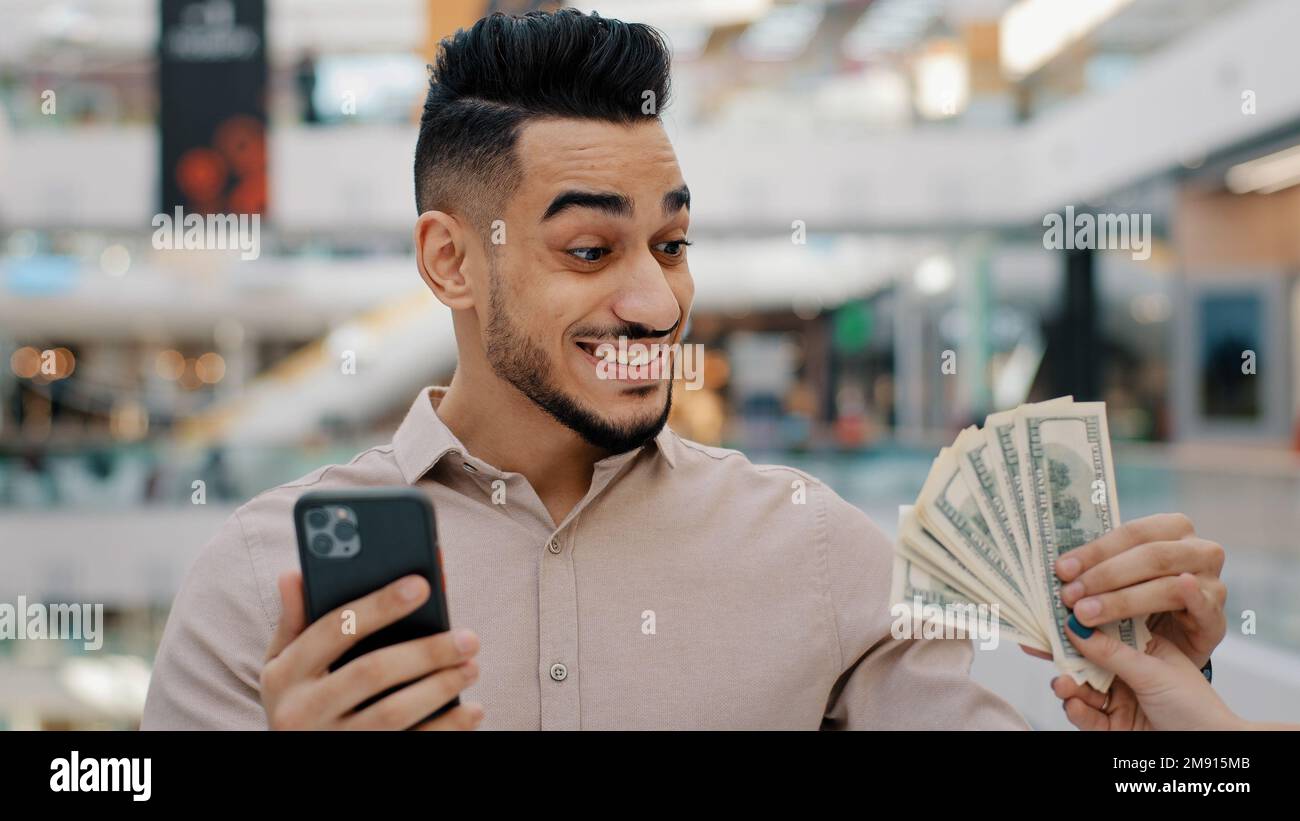 Schockiert überraschter, ethnisch indischer Sieger männlicher Kerl, der mit dem Handy surft, online wettet Casino spielen mit Smartphone, leicht Geld erhalten, verblüfft Stockfoto