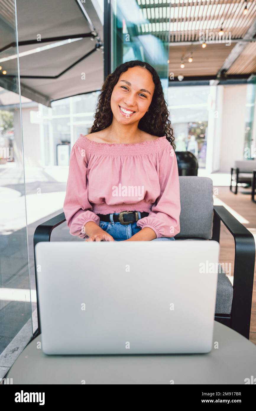 Junge schwarze Studentin, die einen Laptop benutzt und in ihrer Freizeit vor einem Café sitzt. Vertikal Stockfoto