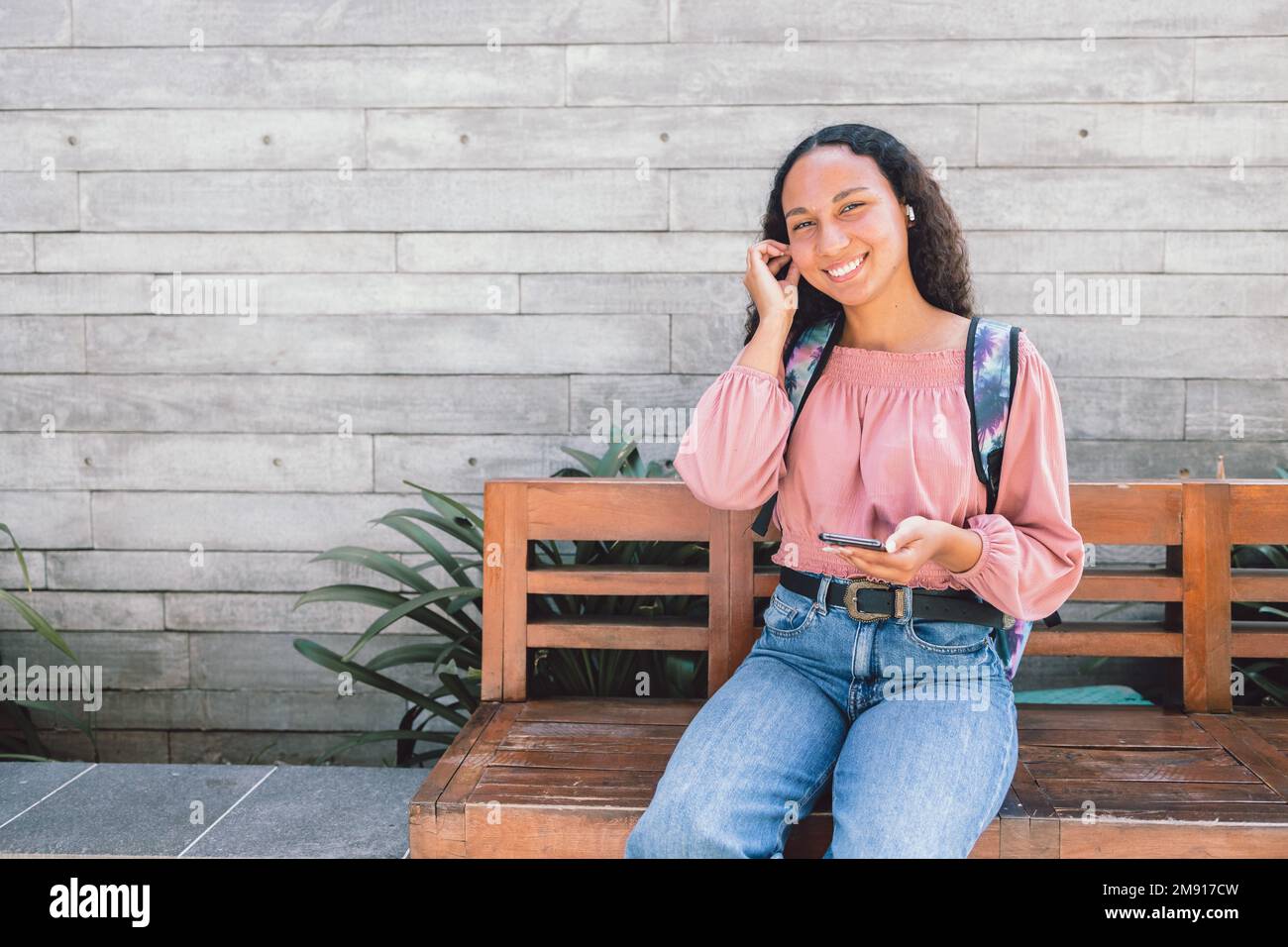 Eine entspannte schwarze Studentin, die auf einer Bank sitzt und soziale Medien auf ihrem Smartphone nutzt Stockfoto