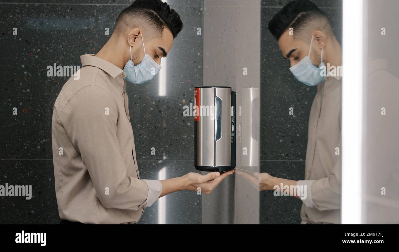 Ethnischer Mann Geschäftsmann Kerl in medizinische Maske im Büro in Flughafen öffentlicher Ort Unternehmen WC Hände waschen mit automatischem Alkohol Desinfektionsmittel Seife Gel Auto Stockfoto