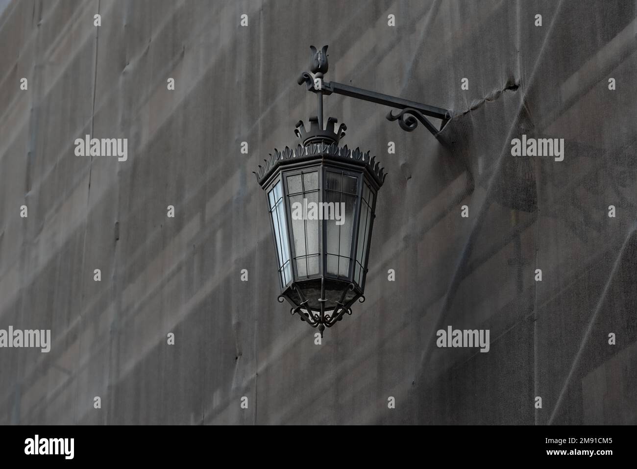 Schmiedeeiserne traditionelle wandmontierte Straßenbeleuchtung, die durch die Schutzleinwand auf einem Gerüst eines Gebäudes in Praca d ragt, das gerade renoviert wird Stockfoto