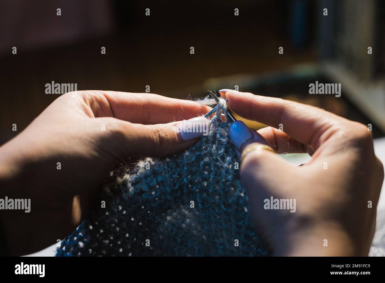 Nahaufnahmen von Händen, die das Kleid aus hellblauer Wolle auf verschwommenem Hintergrund stricken. Mit kreisförmigen Nadeln Stockfoto