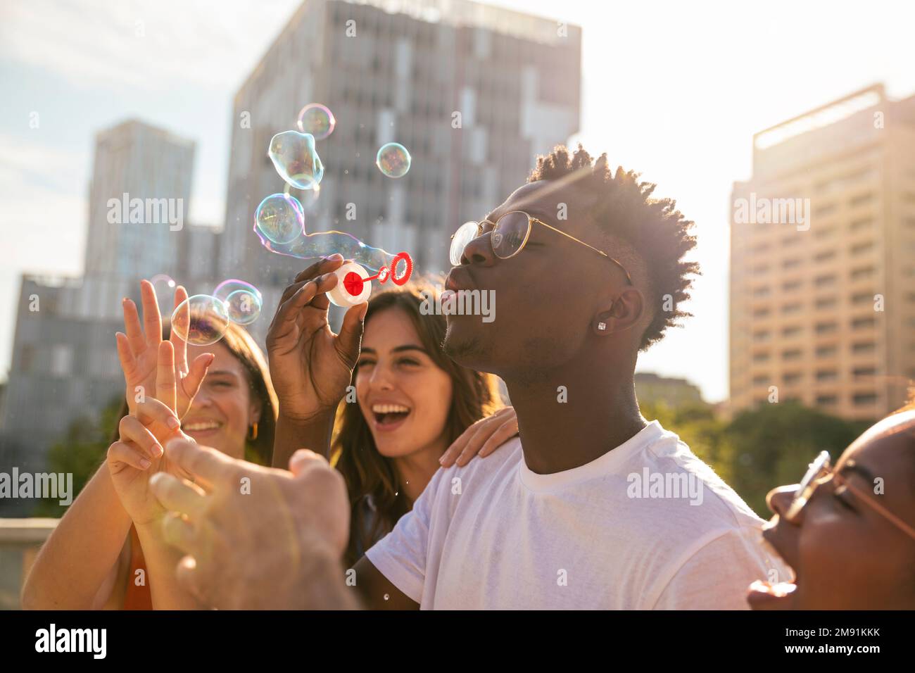 Eine Gruppe multirassischer glücklicher Freunde, die Spaß mit Seifenblasen in der Stadt haben - fröhliche junge Freunde, die an sonnigen Tagen mit Seifenblasen lächeln - Glück Stockfoto