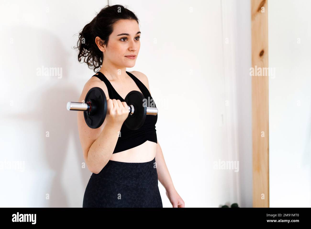 Junge, wunderschöne brünette Frau, die zu Hause trainiert, mit einer Hantelglocke, die fit ist Stockfoto