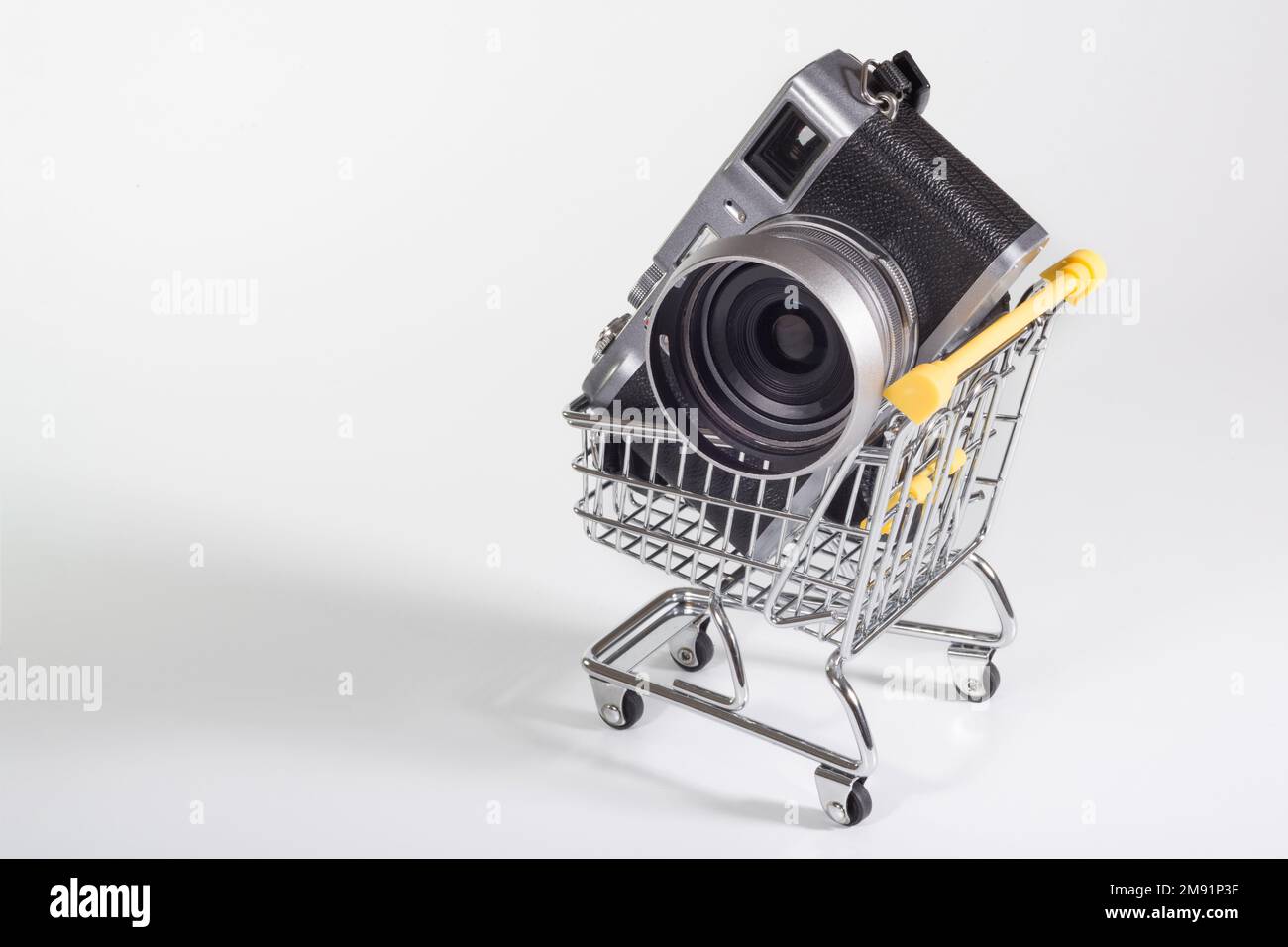 Eine Kamera in einem kleinen Einkaufswagen auf weißem Hintergrund. Verkauf von Fototechniken, Kaufideen. Nahaufnahme Stockfoto