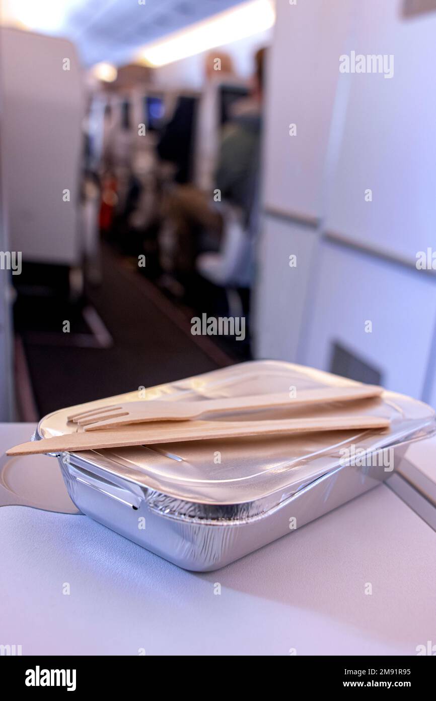 Warme Mahlzeit in einer Folienschachtel mit Holzbesteck auf einem Beifahrer-Tisch in einem Flugzeug Stockfoto