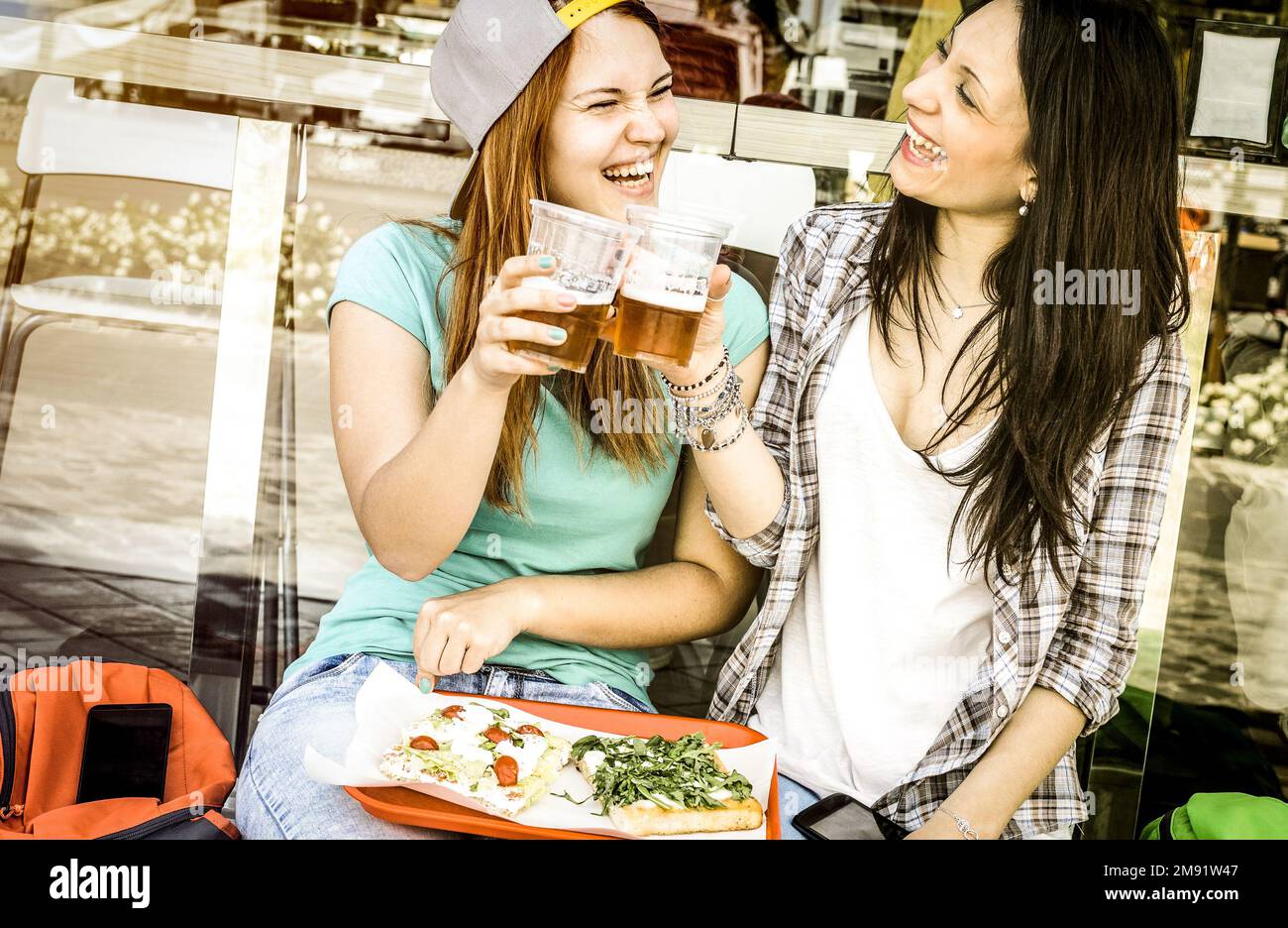 Junge Frauen essen Pizza und trinken Bier im Bar-Restaurant im Freien - Freundschaftskonzept mit glücklichen Freundinnen, die lustige Momente miteinander haben - hübsch Stockfoto