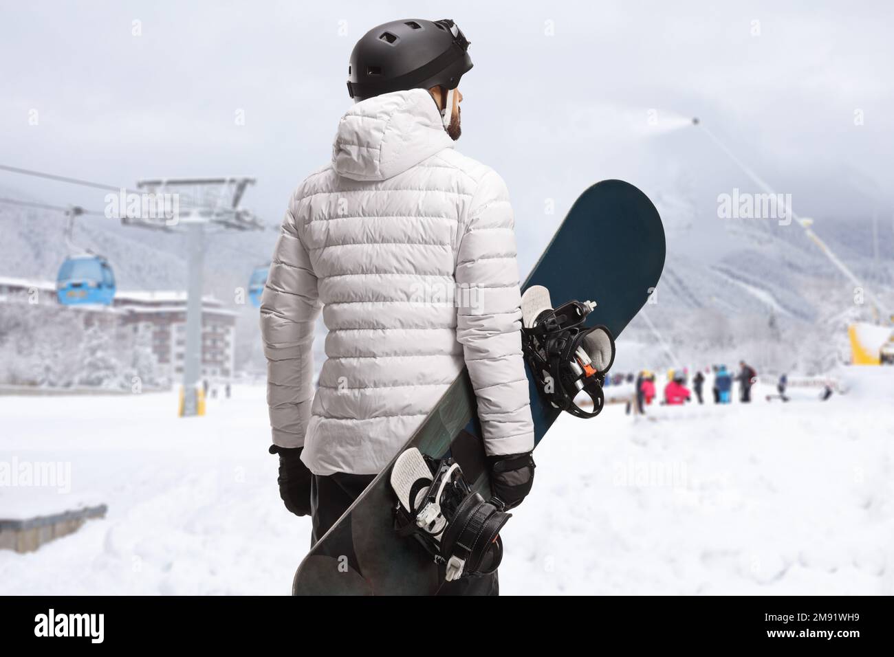 Rückansicht eines Mannes mit Snowboard und Blick auf ein Skigebiet Stockfoto