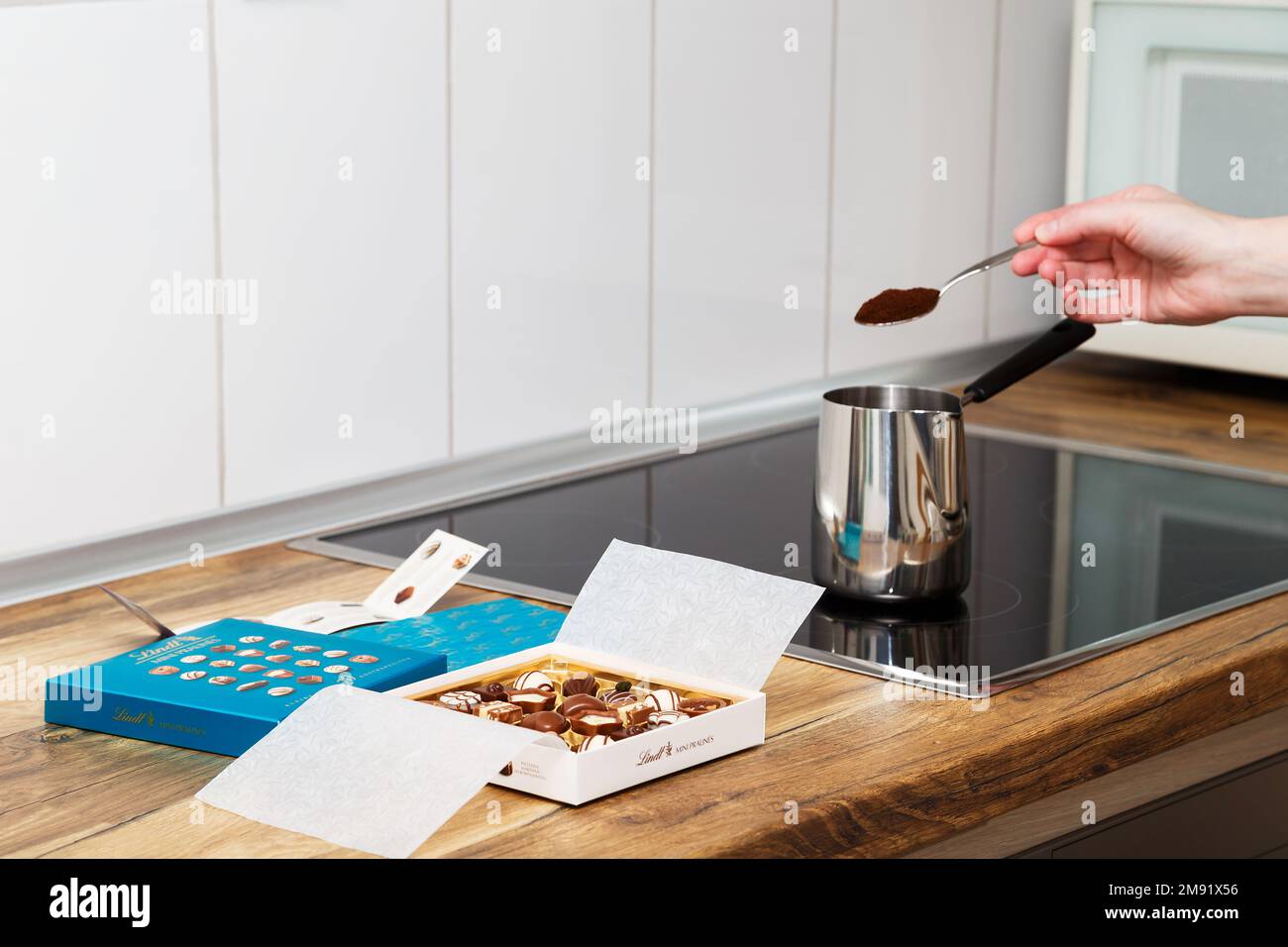 Zürich, Schweiz - Januar 7 2023: Lindt Mini Pralines Box. Offene kleine Geschenkbox mit Schweizer Schokoladensorten und eine Hand junger Frau, die türkischen Kaffee auf der Küchenplatte macht. Stockfoto