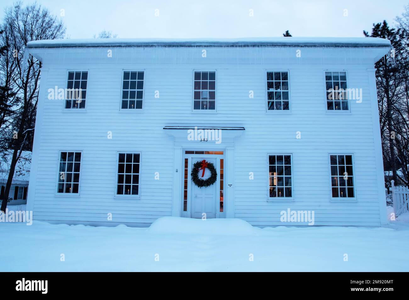 McKusick House wurde um 1846 erbaut, 1969 aus Stillwater, MN, umgezogen, zu Weihnachten mit einem Kranz dekoriert; aufgenommen im blauen Licht eines Winterabends. Stockfoto