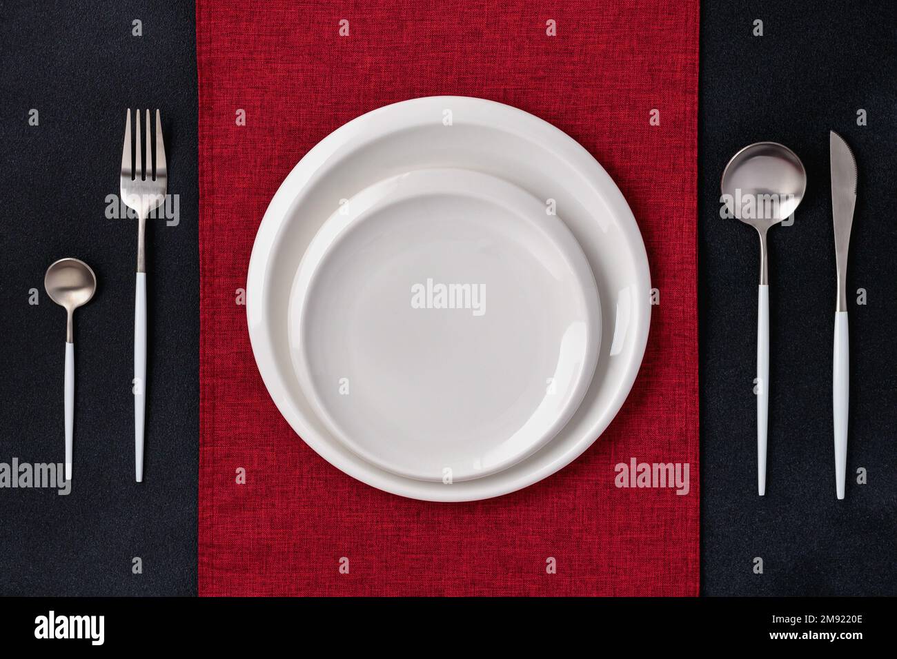 Festliches Ambiente mit roter Serviette. Leere weiße Teller und silbernes Besteck auf schwarzem Hintergrund. Draufsicht. Esstisch im Restaurant. Karte oder Menü t Stockfoto