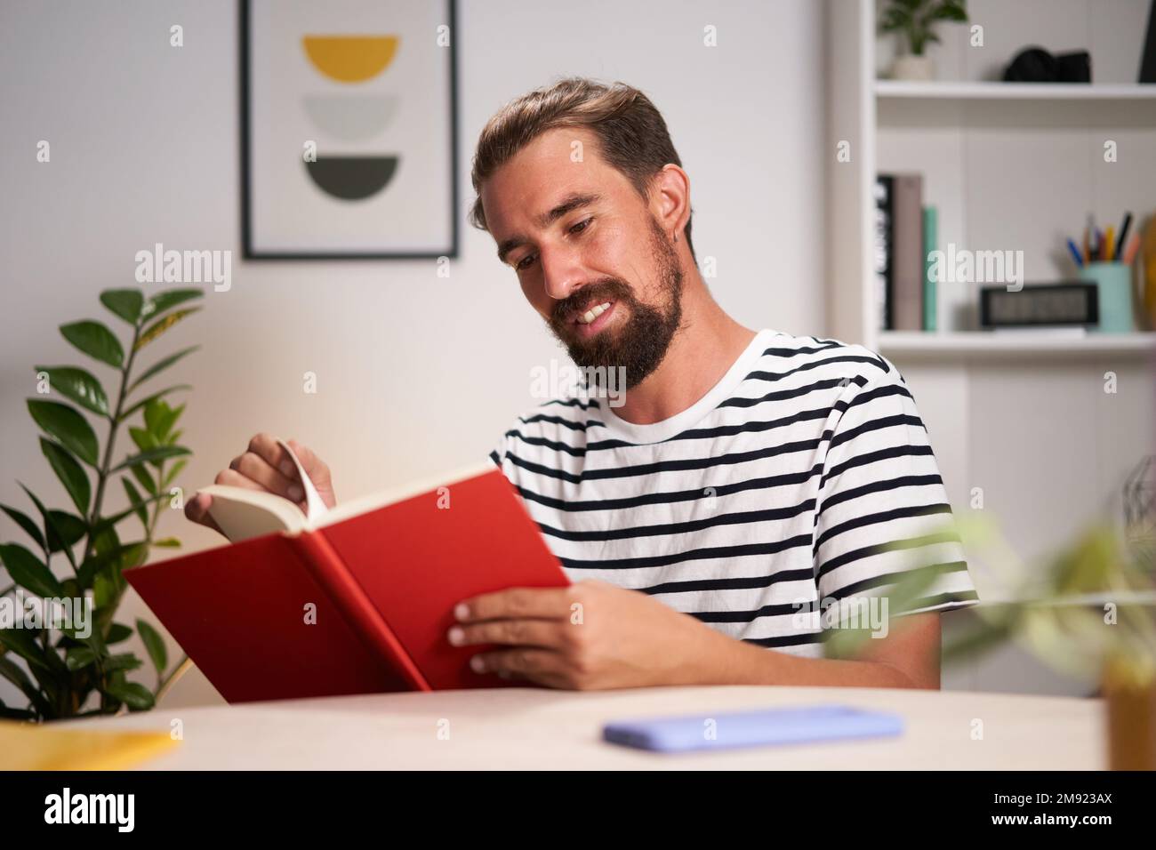 Weißer junger Mann, der zu Hause sitzt, sich konzentriert und ein Buch liest. Stockfoto