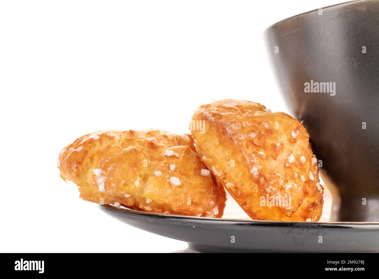 Zwei süße Chouquette mit einer Tasse auf einer Untertasse, Nahaufnahme, isoliert auf Weiß. Stockfoto