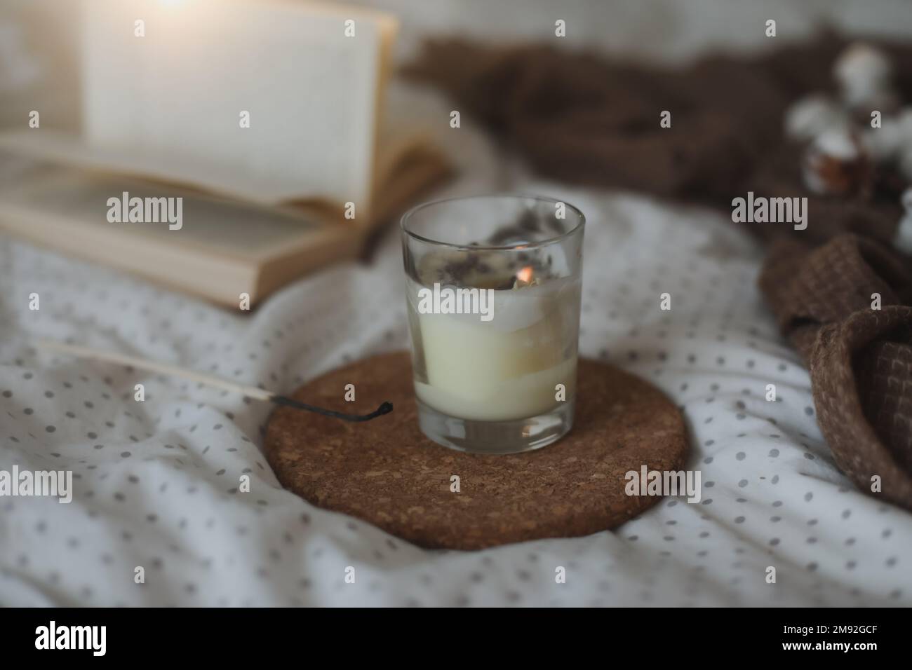 Gemütliche Stille Innenausstattung mit einem Buch, einer Kerze und einem Baumwollzweig in einem warmen, weichen Bett. Süßes Zuhause Stockfoto