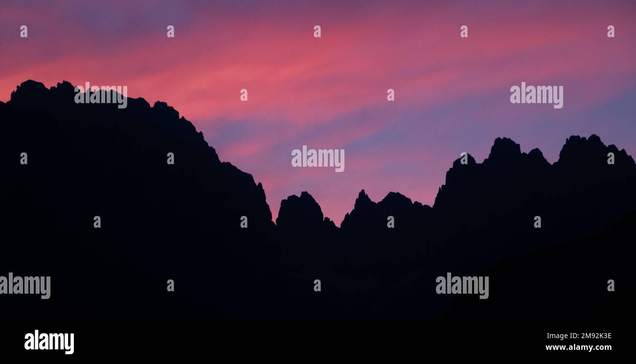 Silhouette einer Gebirgskette in der Abenddämmerung, mit einem wunderschönen Sonnenuntergang aus violetten und rosafarbenen Wolken. Wunderschöne Berge bei Sonnenuntergang in den Dolomiten. Stockfoto